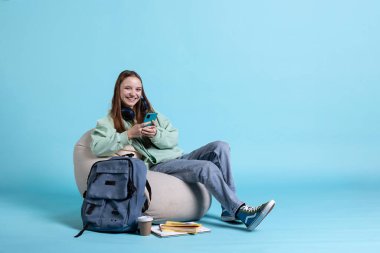 Portrait of jolly young girl reading messages on phone, delighted after receiving good news. Radiant person smiling after receiving positive SMS on smartphone, isolated over studio background clipart