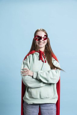 Maskeli, kendine güvenen süper kahramanı kırmızı pelerin giymiş mutlu bir gencin portresi, stüdyo arkaplanı. Kostümlü kahraman kılığına girip kimliğini gizleyen kahraman.