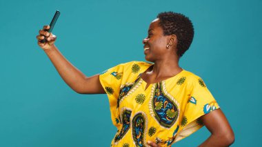 Stüdyodaki resimlerinde mutlu ve heyecanlı olan kadın model, kendine güvenen fotoğraflar çekiyor ve akıllı telefonuyla iyi titreşimler alıyor. Portreler için kendini fotoğraflayan genç bir kadın. Kamera A.