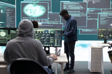 Hükümet hackerları siber tehdit tespiti için verileri analiz ediyor, yüksek teknoloji ofisindeki büyük ekrana bakıyor. Siber istihbaratı, çevrimiçi güvenliği ve dijital tehditlerin önlenmesini vurgula.