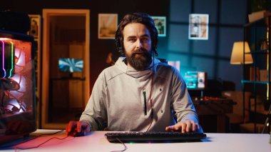 Stüdyodaki neşeli profesyonel oyuncu abonelere canlı yayın sırasında düşmanları yenmek için strateji öğretiyor. RGB 'nin aydınlattığı oturma odasından canlı yayın yapan adam, internet izleyicileri için video oyunları esport rehberini kaydediyor.