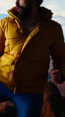 Dikey Video Yürüyüşçüsü dağın zirvesine ulaşır ve başarılı bir tırmanışın ardından zafer pozu verir. Bu da maceraya olan güveni yansıtır. Gezgin fethetmenin kişisel başarısının tadını çıkarıyor.