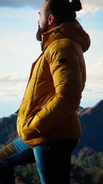 Dikey Video Kaşifi bir dağın zirvesinde duruyor ve temiz hava ve panoramik manzarayı seyrediyor. Yürüyüşçü engebeli tepelerin, engin gökyüzünün, maceranın ve manzaranın çarpıcı manzarasına hayran. Kamera B.