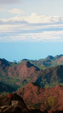 Dikey Video Şiddetli Rüzgârla Savaşan ve daha iyi bir telefon sinyali arayan, dağların tepesindeki akıllı telefonlardan dikkatsiz davranan genç yürüyüşçü. Manzaralı bir tepenin sarp kayalıklarında yuvarlanarak