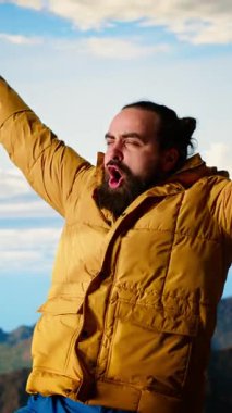 Dikey Video Memnuniyetli Macera Avcısı yükselen bir dağın tepesinde duruyor, destansı manzaranın tadını çıkarıyor ve yürüyüş başarısıyla gurur duyuyor. Güçlü neşeli yürüyüşçü ödüllendirildiğini hissediyor