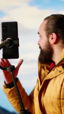 Dikey Video Gezgini vahşi doğada yürüyüş deneyimini kaydediyor. Akıllı telefonuyla sosyal medyadaki macerasını belgeliyor. Arkasındaki güzel manzaralı dağ manzarasını kaydediyor.