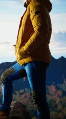 Dikey Video Yürüyüşçüsü dramatik dağ zirveleri ve bulutların panoramik görünümüne bakar, maceranın heyecanını ve azmin ödüllerini hisseder. Yolculuk gücü ve kişisel gelişimi temsil eder.