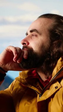 Dikey Video Erkek Aktif Yürüyüşçü, güzel dağ sıraları vadisine hayran ama soğuk rüzgarlarla mücadele ediyor. Kamp alanındaki tehlikeli rüzgarlı havayla mücadele ediyor. Doğada gezinti tutkusu. Kamera B.