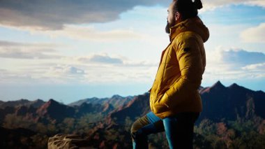 Kaşif bir dağın zirvesinde duruyor ve temiz havayı ve panoramik manzarayı seyrediyor. Yürüyüşçü engebeli tepelerin, engin gökyüzünün, maceranın ve manzaranın çarpıcı manzarasına hayran. Kamera B.