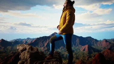 Kararlı gezgin, panoramik manzaranın macera ve kişisel gelişimi temsil ettiği bir dağ zirvesinin yalnızlığının tadını çıkarıyor. Yürüyüşçü rüzgarlı dağın tepesinde üşüyor. Kamera A.