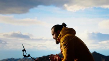 İçerik yaratıcısı, dağlarda açık hava macerasını izleyicileriyle paylaşan bir video bloğu kaydeder. Erkek yürüyüşçü her zaman dengeleyici bir tripoda monte edilmiş bir akıllı telefona bağlıdır. Kamera B.