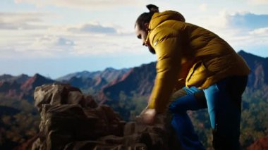 Erkek yürüyüşçü, tepenin zirvesinden nefes kesici bir dağ sırasına bakar ve büyük açık havanın yalnızlığını ve temiz havasını kucaklar. Macera hissi ve sonsuz doğa keşfi. Kamera A.