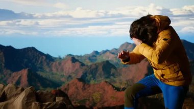 Şiddetli rüzgarla savaşan ve daha iyi bir telefon sinyali arayan genç yürüyüşçü, dağın tepesindeki akıllı telefon tarafından dikkatsiz davranıyordu. Manzaralı bir zirvenin sarp kayalıklarında yuvarlanarak. Kamera B.