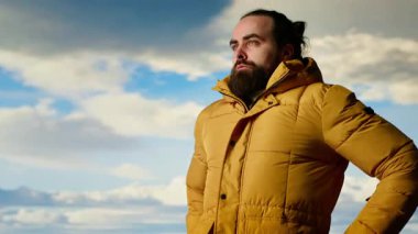 Doğa aşığı nefes kesen bir dağ sırasının kenarında duruyor, yükselen zirvelerin ve uçsuz bucaksız gökyüzünün manzaralı arka planına bakıyor. Macera ve açık hava keşiflerini seven genç bir adam. Kamera B.