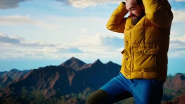 Erkek doğa aşığı dağın tepesinde soğuk rüzgarla boğuşuyor, kayalık tepelere tırmanıyor ve üşüyor. Genç yürüyüşçü maceracı manzaranın tadını çıkarıyor. Kamera A.