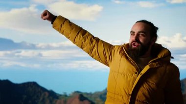 Macera Avcısı nefes kesici bir manzara için yüksek bir yükseklik dağının tepesinde duruyor. Yürüyüşçülerin kollarını kaldırmasından ve sevinçten çığlık atmasından memnun. Korkuları ve zorlukları yenmek. Kamera B.