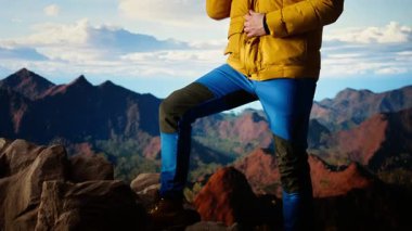 Dağ yürüyüşçüsü, zirveye tırmandıktan sonra geniş bir tepe ve gökyüzü manzarasıyla ceketinin fermuarını çekerek vahşi doğada gezinti macerasını kucaklıyor. Açık hava keşfi. Kamera A.