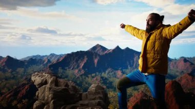 Macera Avcısı nefes kesici bir manzara için yüksek bir yükseklik dağının tepesinde duruyor. Yürüyüşçülerin kollarını kaldırmasından ve sevinçten çığlık atmasından memnun. Korkuları ve zorlukları yenmek. Kamera A.