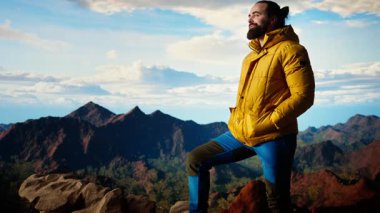 Sıcak giysili maceraperest, vahşi doğanın huzurundan, panoramik dağ manzarasından ve açık gökyüzünden keyif alır. Rahatlamak için mükemmel bir ortam yaratır. Soğuk rüzgarlar yokuş yukarı. Kamera A.