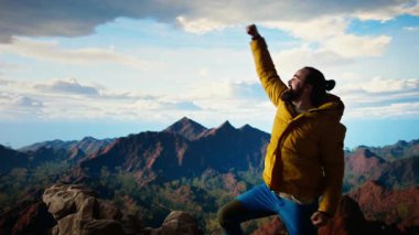 Açık hava kıyafetleri giymiş yürüyüşçü dağın zirvesine ulaşmasını kutluyor. Çarpıcı bir manzara ve tatmin duygusu macera ve kişisel gücün heyecanını temsil ediyor. Kamera A.
