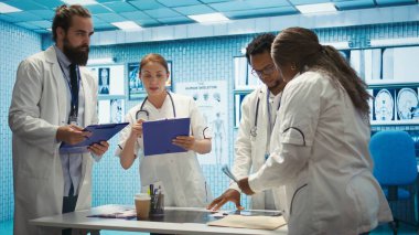 Özel bir klinikte teşhis verilerini analiz eden ve tedaviyi planlayan bir grup sağlık çalışanı, işbirliğini vurguladı. Son test sonuçlarından sonra kurtarma planlarını koordine ediyorum. Kamera B.