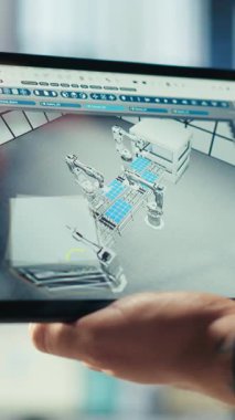 Fotovoltaik fabrikasındaki dikey video mühendisi, güneş panelleri üreten robotların performansını gözden geçirmek için tablet üzerindeki izleme yazılımını kullanır. Uzman, güneş santrali makinelerini denetlemek için aygıt kullanıyor