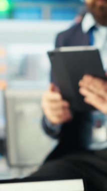 Dikey video Photovoltaics fabrikası çalışanı, güneş panellerini montaj hatlarına yerleştiren robotların performansını gözden geçirmek için tablet kullanıyor. Masada oturan uzman, güneş santralini incelemek için aygıt kullanıyor.