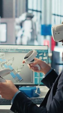 Dikey video Photovoltaics fabrika işçisi, robotların güneş panellerini montaj hatlarına yerleştirme performansını izlemek için VR kulaklık kullanıyor. Sanal gerçekliği kullanarak güneş santrali makinelerini denetleme uzmanı