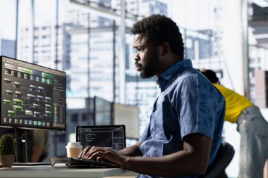 Veri bilimci, karar verme süreçlerini geliştirmek ve otomatikleştirmek için veri işleyebilen makine öğrenme modelleri yaratıyor. Afrika kökenli Amerikan bilişim uzmanı bilgisayar kullanarak ofisinde programlama yapıyor.
