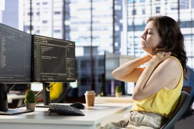 Uygulama sorunları düzeltilirken boyun ağrısı çeken geliştirici, veritabanı ve sunucu yapılandırması ile ilgileniyor. Şirket yazılımını optimize ederken çok çalışan yorgun bir kadın.