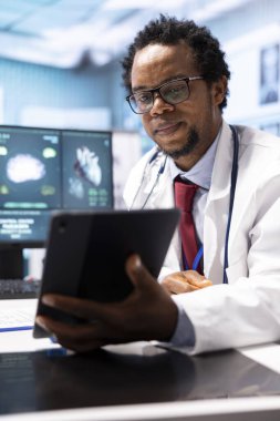 Afro-Amerikalı doktor, röntgen testlerini tabletle sunuyor. Test sonuçlarını ve sağlık analizlerini açıklıyor. Tıbbi personel, iyileşme sürecinde bir kadına destek oluyor..