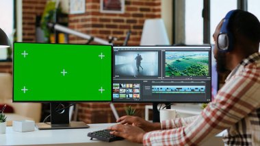 Erkek film yapımcısı, bir video projesini fotokopi ekranı kullanarak modern bir renk derecelendirme yazılımında düzenliyor. Genç adam video yapımının yaratıcı sürecinde çift monitörlerde çalışıyor. Kamera B.