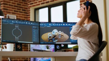 Asyalı profesyonel mühendis gelişmiş yazılım araçları kullanarak endüstriyel tasarımlar üzerinde çalışıyor. Oturma odasında çift monitörler ve yüksek verimlilik için teknik ekipmanlar var. Kamera B.