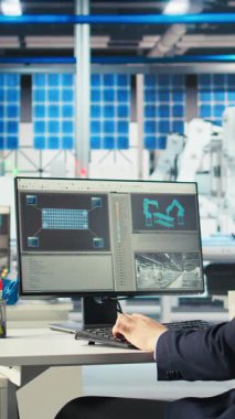 Robot kolların montaj hatlarına güneş panelleri yerleştirme performansını izlemek için PC kullanan dikey video Photovoltaics fabrikası çalışanı. Bilgisayar masasında uzman. Ekrana bakıyor, güneş santralini inceliyor.