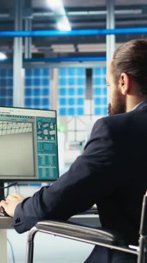 Tekerlekli sandalyedeki paraplejili dikey video Photovoltaics fabrikası çalışanı güneş paneli imalatının performansını izlemek için bilgisayarı kullanıyor. Güneş santrali makinelerini denetleyen engelli kişi