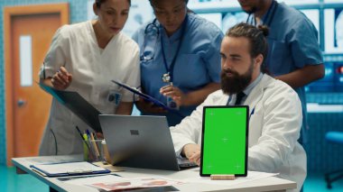 Krom anahtar ekranının yanındaki hastane kayıtlarına bakan bir grup doktor teşhisi incelemek için x ışını test sonuçlarını kullanıyor. Çeşitli uzmanlar tedavi planı için özel klinikte toplanıyorlar. Kamera A.