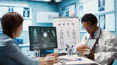 Afrika kökenli Amerikalı bir uzman, hastaya teşhis koyan insan iskeletini gösteriyor. X ışını görüntüleme taraması yorumu. Tıbbi uzman laboratuvar sonuçlarını kabinede inceliyor. Kamera B.