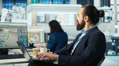 Yenilenebilir enerji fabrikasında çalışan robot kolların güneş panelleri yerleştirme performansını incelemek için dizüstü bilgisayar kullanıyor. Uzman, güneş hücrelerini taşıyıcı bantlara yerleştiren makineleri inceliyor, kamera B