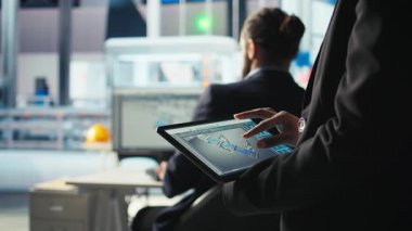 Fotovoltaik fabrikası uzmanı CAD uygulamasında tablet kullanarak üretim hatları tasarlıyor. Güneş panelleri fabrika teknisyeni, üretim planlarını optimize etmek için aygıt üzerinde simülasyon yazılımı kullanır.