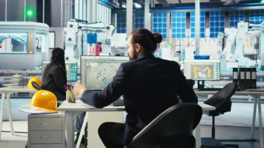 Fotovoltaik fabrikası mühendisi sistem parametrelerini ayarladıktan sonra performans notları alıyor. Güneş paneli üretim tesisinde enerji arzını optimize etmek için teknisyen yazma ayarlaması