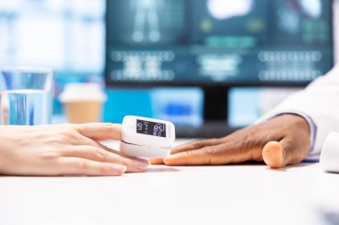 Genel pratisyen bir hasta için oksijen doygunluğunu ve hayati belirtileri ölçer ve kabine ofisindeki diğer teşhis araçlarını kullanır. Erkek uzman bir kadına danışmanlık yapıyor, sağlık hizmetleri..