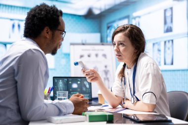 Sıcaklık ölçümlerini kontrol etmek için termometreyi kullanan bir sağlık uzmanı. Tıbbi konsültasyonda sıcaklık seviyelerini ölçüyor. Tanısal raporlar için dijital araç kullanan genç doktor.