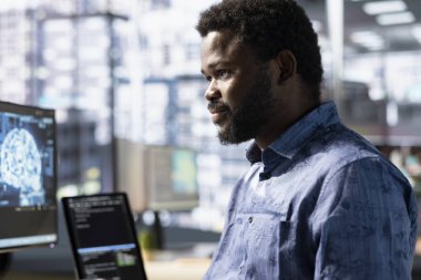 Büyük ölçekli makine öğrenme modellerini eğitmek ve uygulamak için yapay zeka bulut kaynaklarını ve platformları kullanan neşeli bir çalışan. Gülümseyen Afrikalı Amerikalı adam şirket sistemlerini izliyor ve koruyor.