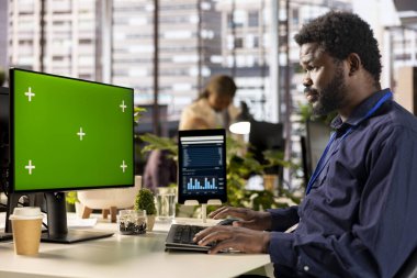 Ofis masasındaki siyah işadamı, başarı için etkili karar verme sürecini desteklemek amacıyla analitik ve bilgi grafikleri üzerine çalışan yeşil ekranın yanındaki günlük işlerde çalışıyor. İş işlemleri.