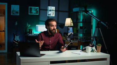 Selfie çubuğunda akıllı telefon kullanarak video çeken, çılgın hareketler yapan etkileyici bir adam. Stüdyoda telefonla video bloğu çekerken hareketli el hareketleri yapan canlandırıcı, kamera B