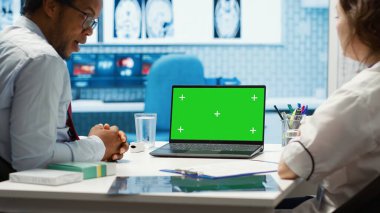 Tıbbi uzman, kabinede izole edilmiş kroma anahtar görüntüsünü işaret ederek hastalık teşhisi ve test analizi için tarama yapıyor. Profesyonel doktor hastasını destekliyor. Kamera A.