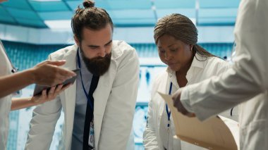 Sağlık ekibi potansiyel tehlikeli teşhisler için test sonuçlarını inceliyor, toplantı sırasında radyografi taramalarına bakıyor. Radyoloji alanında uzman doktorlar hastalık önleme üzerinde çalışıyorlar. Kamera A.