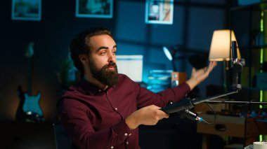 Stüdyoda selfie çubuğuna bağlı cep telefonuyla barış işareti yaparak izleyicilerle mikrofon kullanarak sohbet ediyor. Adam el hareketi yapıyor, telefon ve mikrofonu kullanarak vlog kaydediyor, kamera A