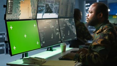 Askeri ajan kontrol odasında çalışıyor, yeşil ekran cihazları üzerinde yazılım kullanıyor, hava keşif verilerini analiz ediyor. Krom anahtar sistemli İHA 'ları kontrol eden istihbarat birliği uzmanı, kamera A