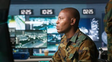 Askeri üste dijital radar ekipmanları ve çalışan füze sistemleri ile gözetleme yapan bir istihbarat ajanı. Afrika kökenli Amerikalı bir adam, ordu merkezinin güvenlik kameralarını, izinsiz hareketler için izliyor. Kamera A.